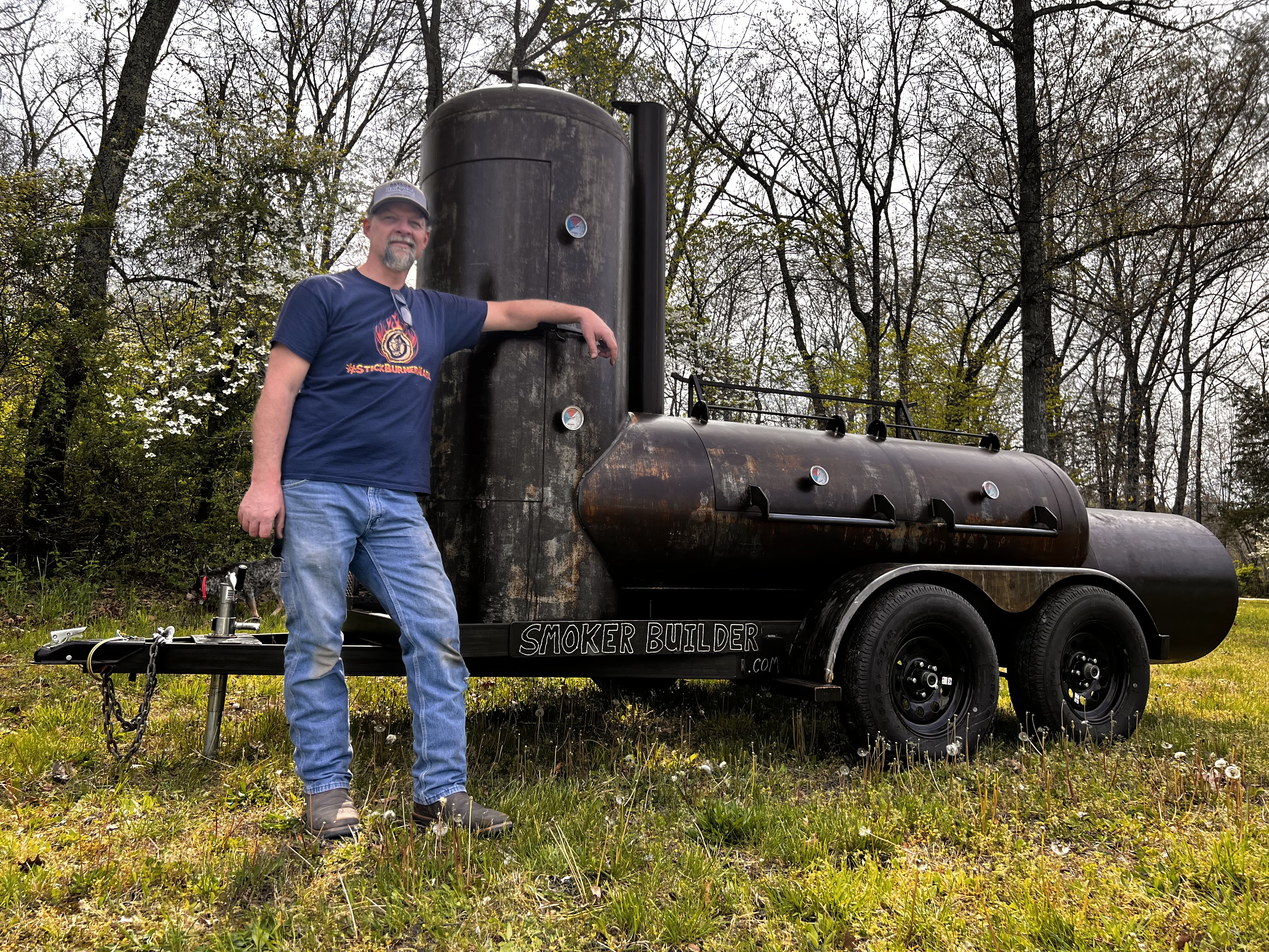 Frank Cox standing next to a finished propane tank offset smoker on a tandem axle trailer