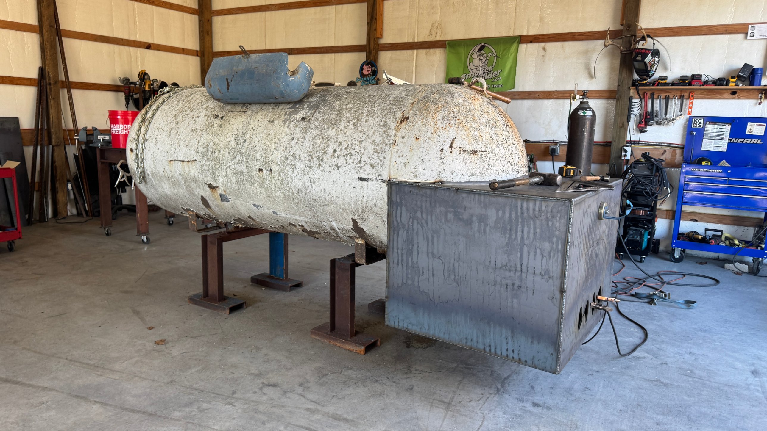 Square firebox tacked onto the end of a propane tank sitting on stands in the shop