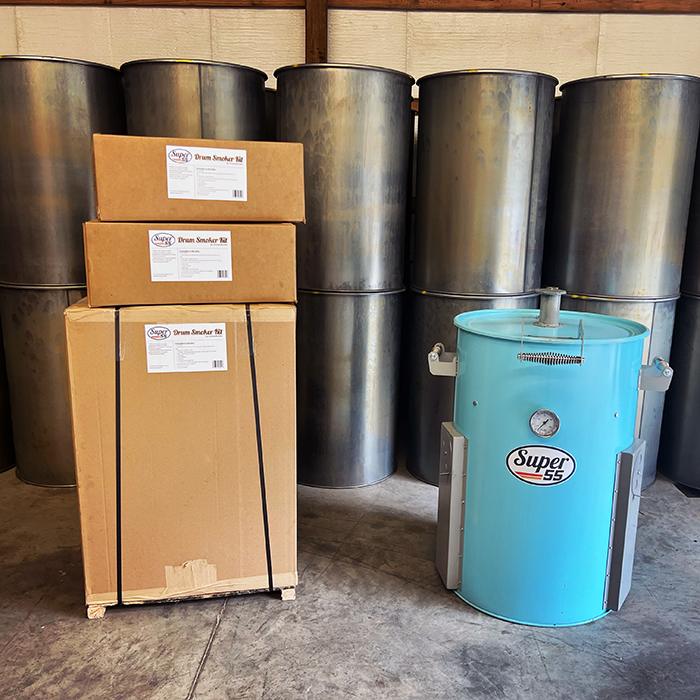 cardboard boxes stacked up on left side of picture with a light blue barrel smoker and bare steel barrels stacked in the background