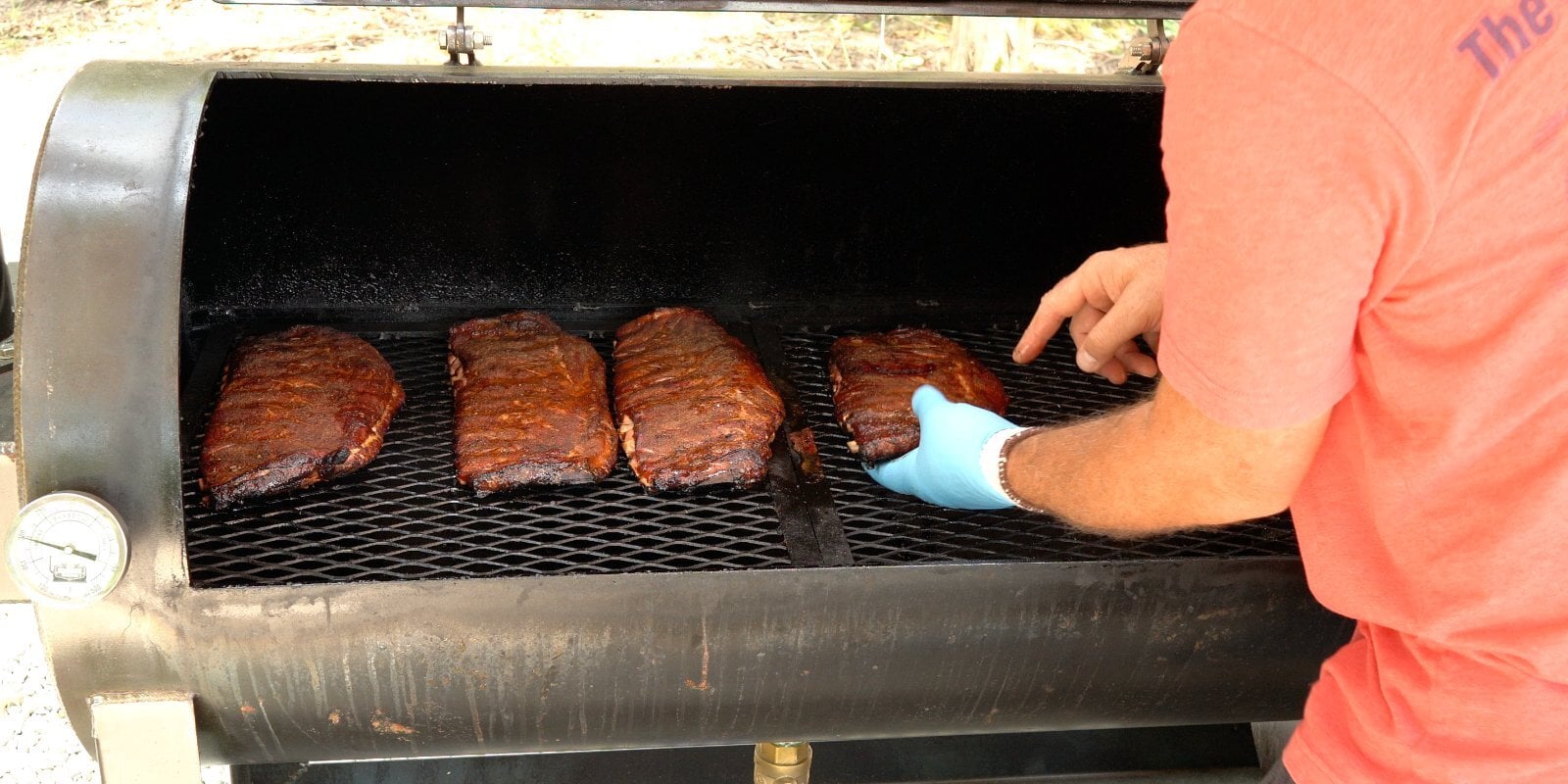 Four racks of ribs spread across the cooking grate of an offset smoker