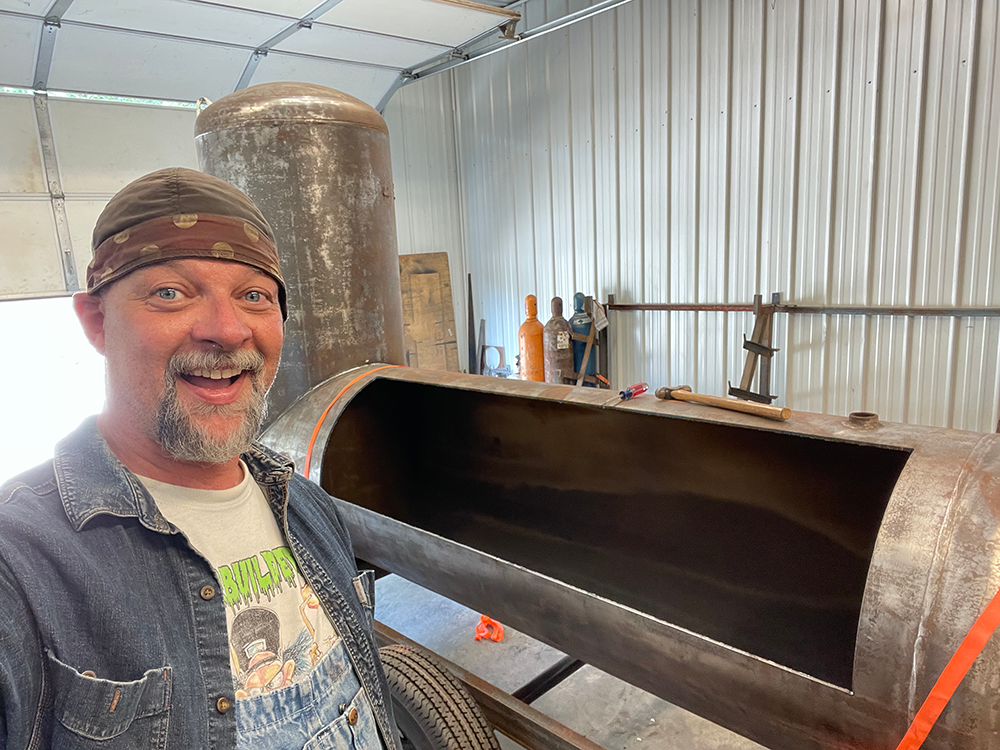 Frank Cox next to a tank smoker with the cook chamber doors cut out
